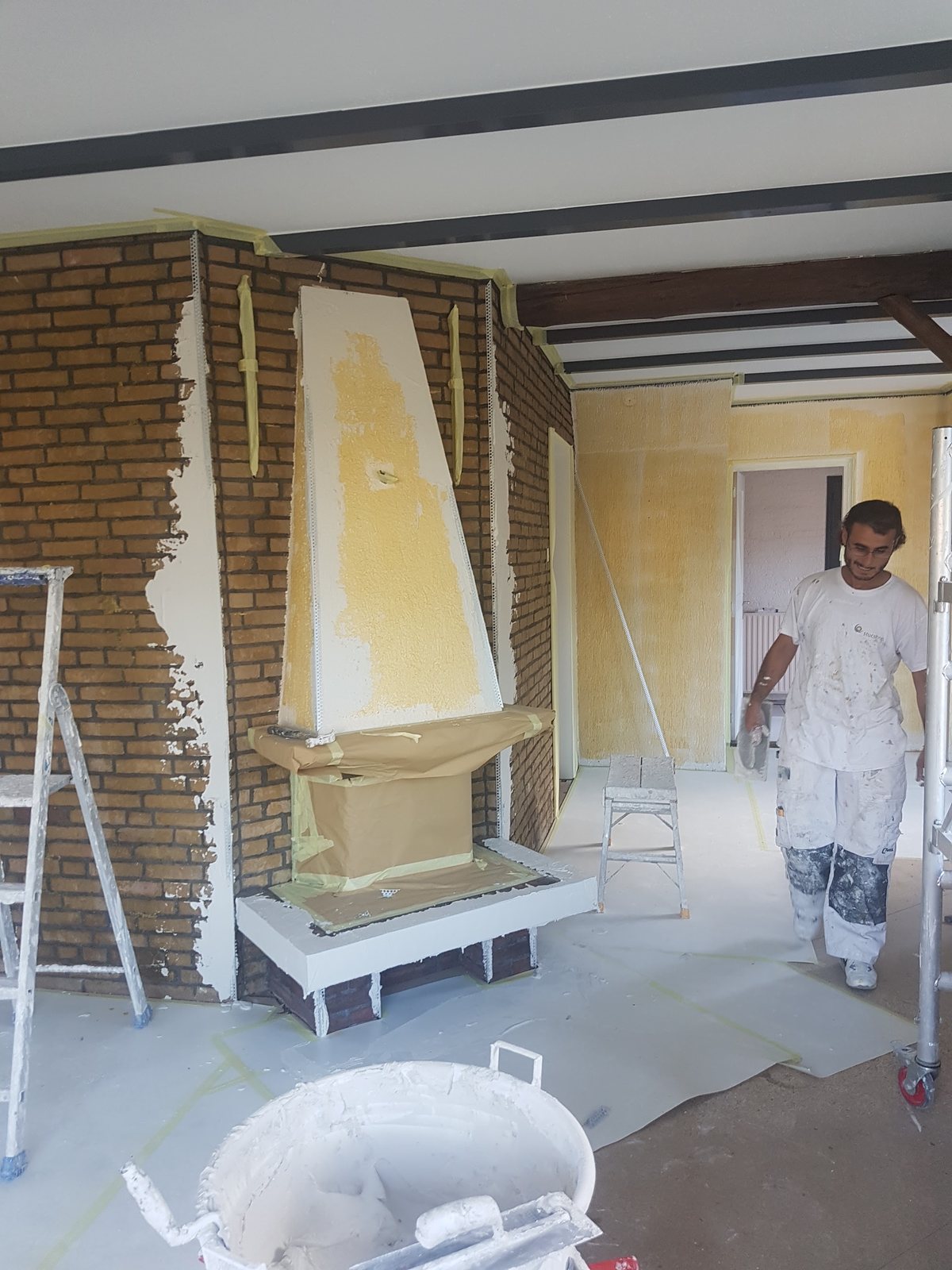 Schouw in de gele grondlaag, met een stukadoor in witte werkkleding en een kuip