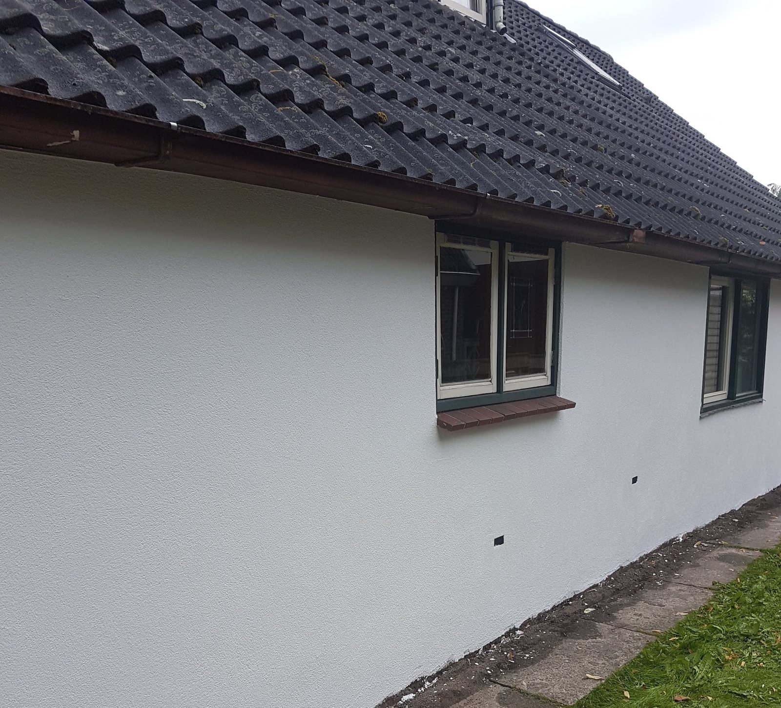 Lange witte gestucte muur van een bungalow met donker pannendak